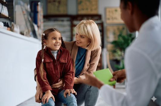 A smiling young girl and her mother consulting with a pharmacist in a pharmacy. The pharmacist is gesturing toward a product, illustrating a supportive and professional guidance session for childhood eczema management.